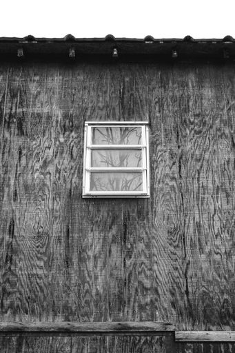 A grayscale shot of the old wooden house with a small window in the village on a gloomy day