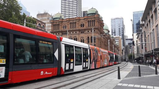 A tram traveling through a street in Sydney with the Queen Victoria Building in the background