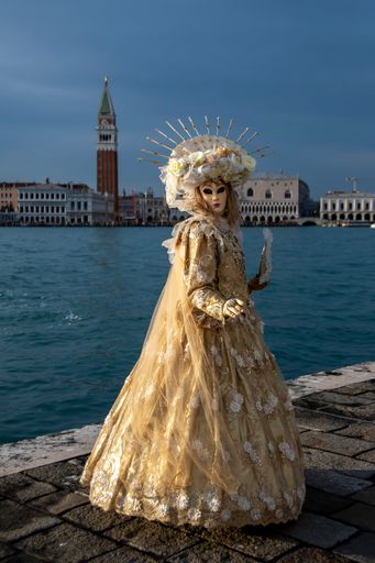 A vertical shot of a woman in carnival clothing standing on the shore with the city in the background
