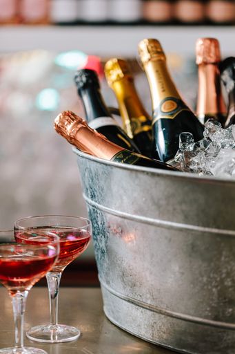 A vertical shot of a bucket filled with ice and champagne near two cocktails on the counter