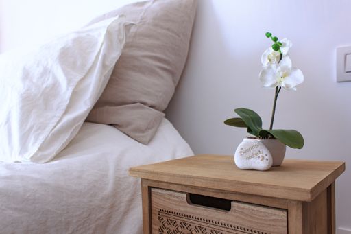 A closeup shot of a wooden nightstand with a small plant in a pot and a good night text in Spanish