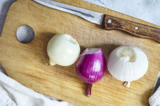 An overhead shot of three onions on the cutting board next to the knife