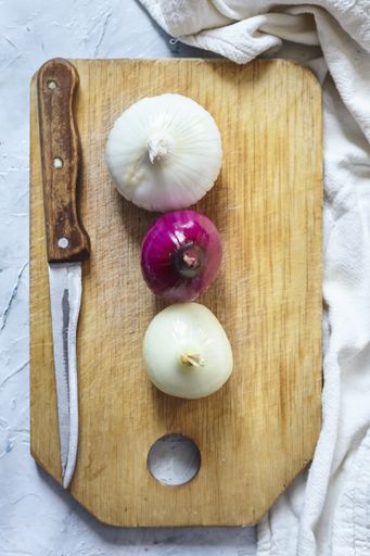 A top view of peeled white and purple onions with a knife on a wooden board