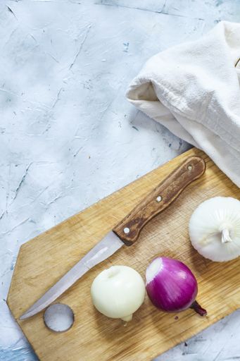 A vertical shot of three onions on the cutting board next to the knife