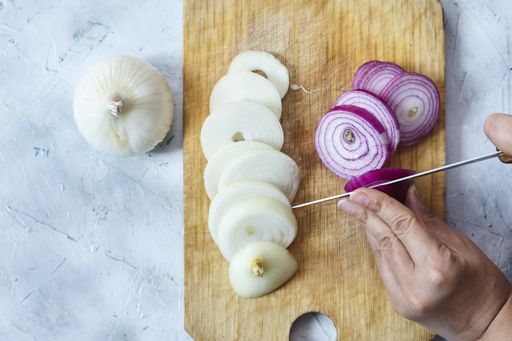A top view of a person slicing purple and white onions on a slicing board