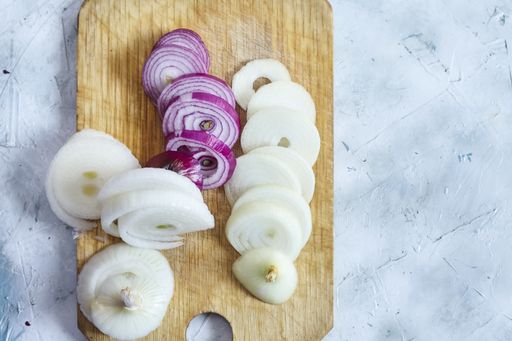 A top view of sliced purple and white onions on a slicing board