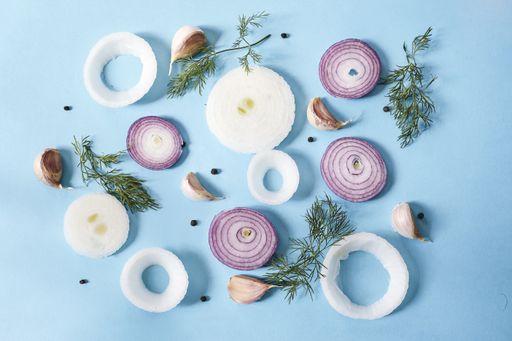 A top view of raw onion rings with peppercorns, garlic and dill on a blue surface