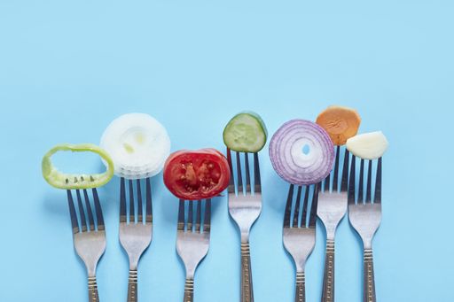 A top view of sliced pieces of fresh vegetables and spices on forks against a blue background