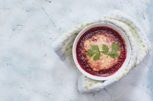 A top view of beetroot and carrot soup with feta cheese in a bowl with a kitchen towel wrapped around it