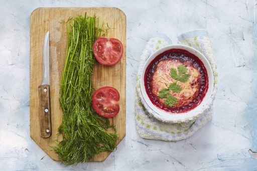 A salad of mashed potatoes and tomato sauce next to greens and tomatoes on a cutting board