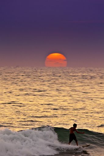 A vertical shot of a male surfing in the sea during sunset under the beautiful colorful sky