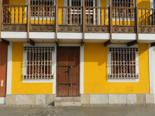 A two-story house with a wooden door and windows in a yellow wall
