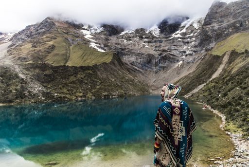 A man in colorful poncho standing in front of a beautiful view of a crystal lake in Mountain Machu Picchu in Peru