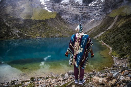 A man in colorful poncho standing in front of a beautiful view of a crystal lake in Mountain Machu Picchu in Peru