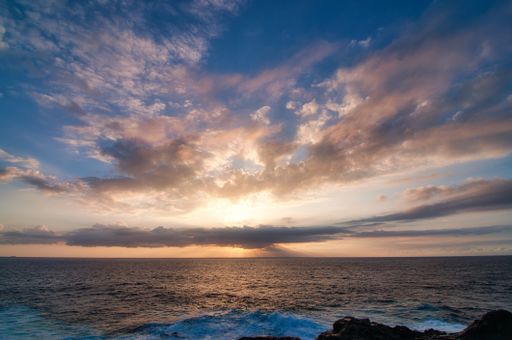 A beautiful view of an ocean with a glowing sun and a cloudy sky in the background