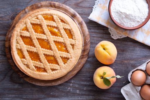 A top shot of apricot pie with fresh eggs and a bowl of flour in a wooden surface