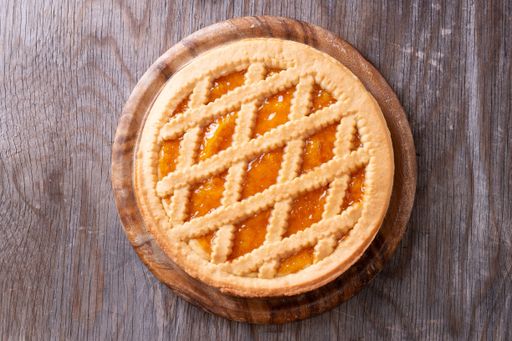 A top shot of apricot pie with fresh eggs and a bowl of flour in a wooden surface