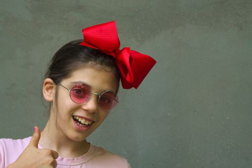 A closeup shot of a young Caucasian female with red bow on head showing thumb up and smiling at camera