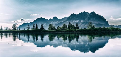 A panoramic shot of a beautiful scenery with rocky mountains and fir trees reflected in the lake