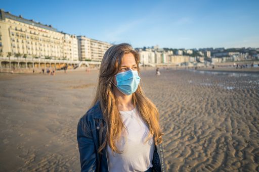 A horizontal shot of a young caucasian female with a medical mask posing on an urban sandy beach