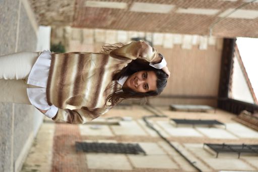 A vertical shot of a Caucasian brunette in an alley with her hand in her hair smiling at the camera