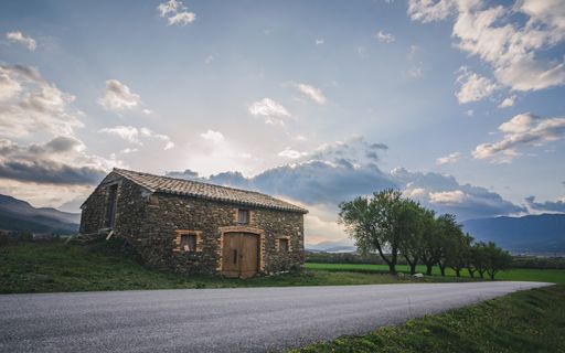 A beautiful landscape with a small stone house near a road under a cloudy sky
