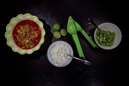 A high angle shot of the delicious soup, sliced green chili peppers and onions in the white bowls, limes and green squeezer on a black background