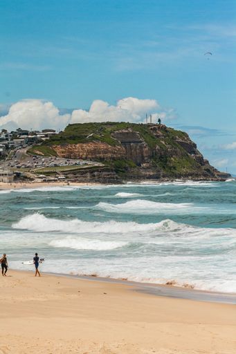 A vertical shot of surfers in a sandy beach near the wavy ocean on a sunny day in Newcastle,Merewether
