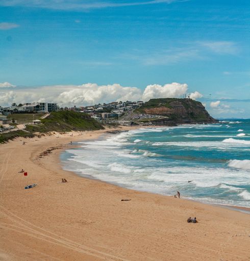 A scenic view of sandy beach and blue wavy ocean on a sunny day in Newcastle, Merewether