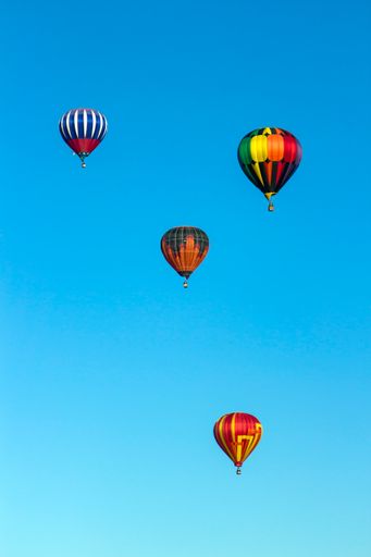 A vertical shot of 4 hot air balloons in the blue sky during Albuquerque International Balloon Fiesta, 2019