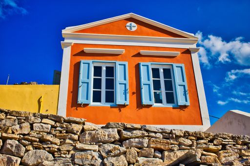 A low angle shot of an orange house with blue windows with the background of blue cloudy sky in Greece