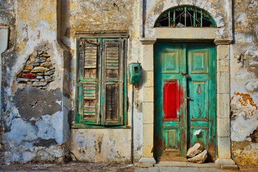 A horizontal shot of an ancient green wooden door and a window on an old yellow wall in Greece