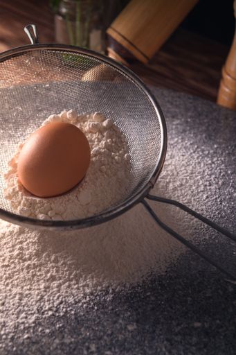 A vertical high angle shot of an egg on flour on a wooden table