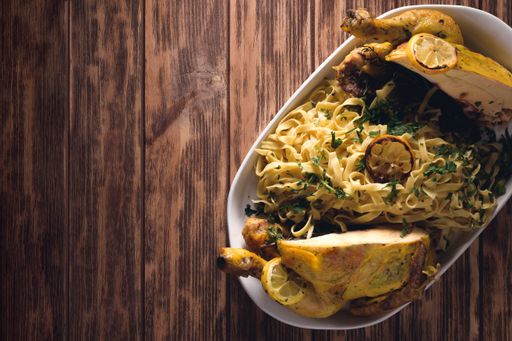 A top view of a roasted chicken with Fettucine pasta on a white plate