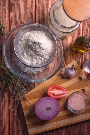 A top view of a flour surrounded with ingredients on a wooden table