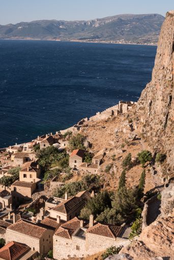 A vertical shot of coastline with buildings near the sea surrounded by high mountains