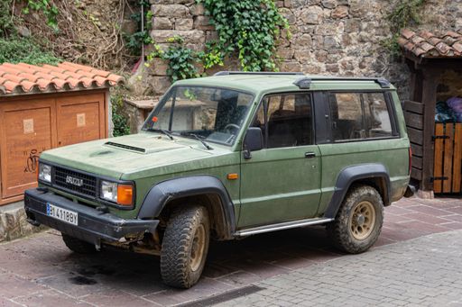 An old town off-road car parked on the street is painted camouflage green. Isuzu Trooper