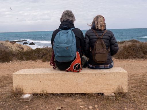 A closeup shot of a Caucasian and a woman sitting on the wooden desk and looking at the sea