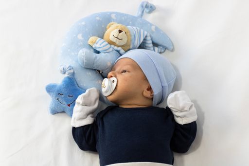An adorable newborn baby boy lying in the bed with his toys