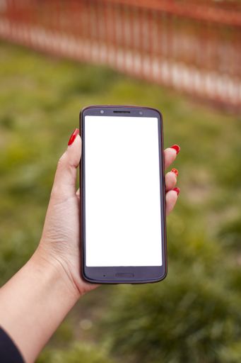A vertical shot of a female with red nail polish holding a phone with a blank screen