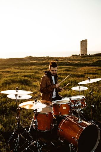 A vertical shot of a young man playing drums in a green field