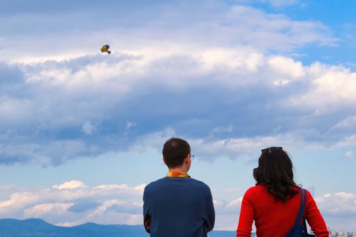A man and a woman looking at the beautiful blue sky with fluffy clouds captured from behind