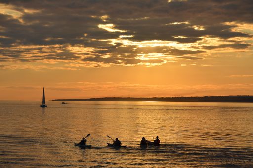 A beautiful view of a sunset over the sea with people swimming with small boats