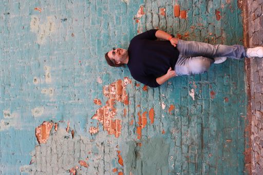 A Caucasian man in sunglasses leaning back to a blue brick wall