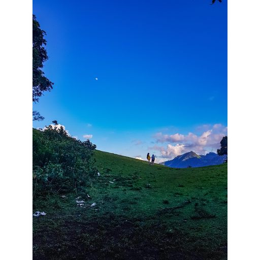 A view of tourists on a hill looking at mountains under the blue sky