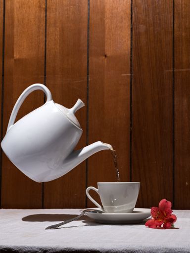 A vertical shot of tea pouring from a teapot into a cup on the table under the lights