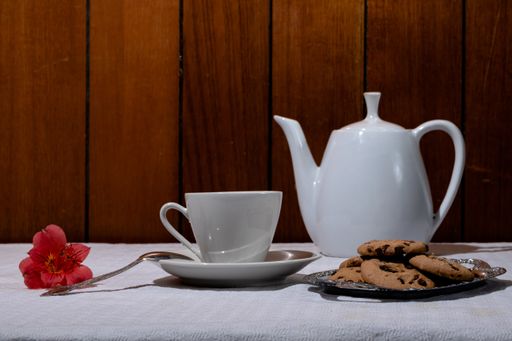 A closeup of a cup and a teapot with chocolate chip cookies on the table under the lights