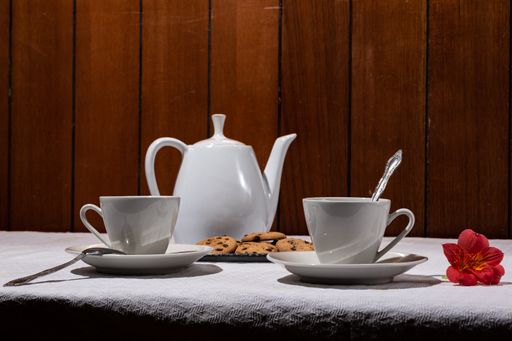 A closeup of a ceramic teapot with cups and chocolate chip cookies on the table under the lights