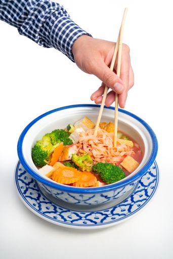 A vertical shot of a man holding chopsticks in a Thai Tofu Veggie dish in a traditional Thai bowl