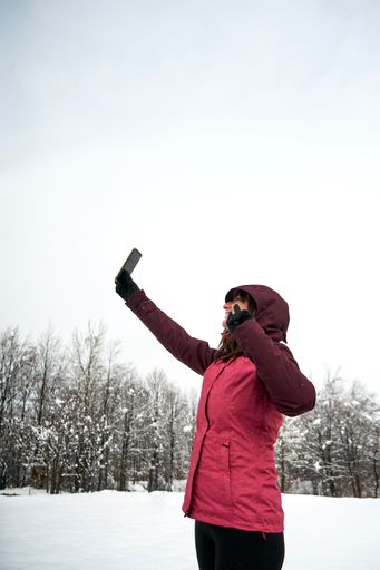 A vertical shot of a Caucasian woman in pink warm clothes taking selfies in winter under snow